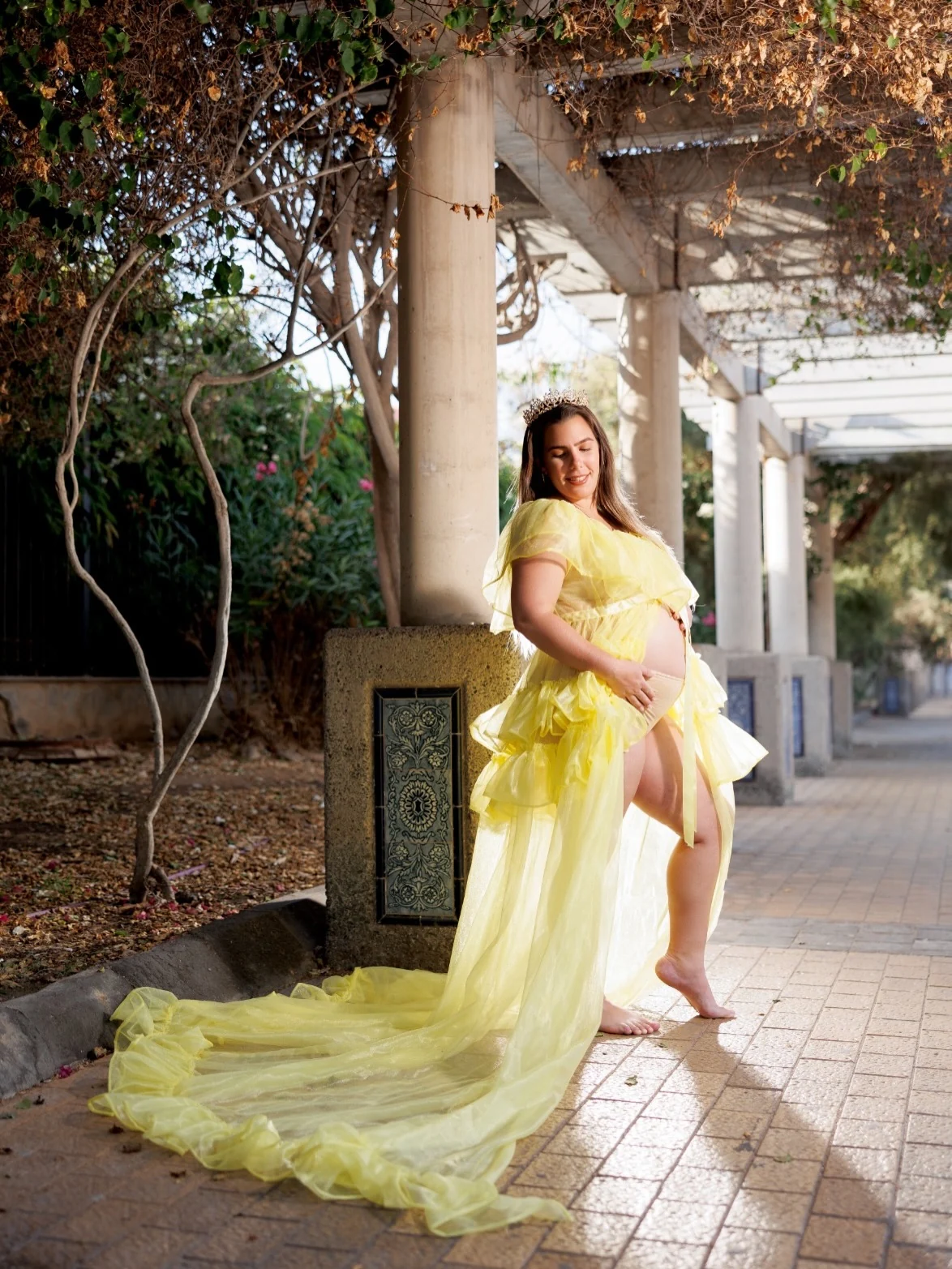 Embarazada con vestido amarillo junto a una pérgola