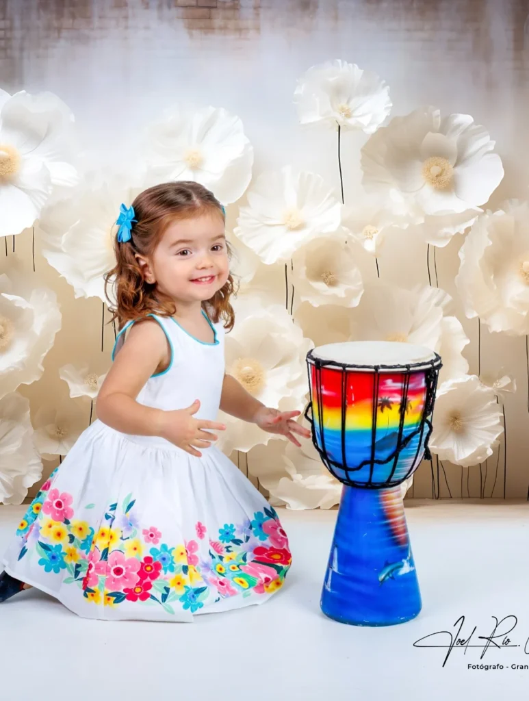 Niña con vestido blanco y tambor de colores en el estudio