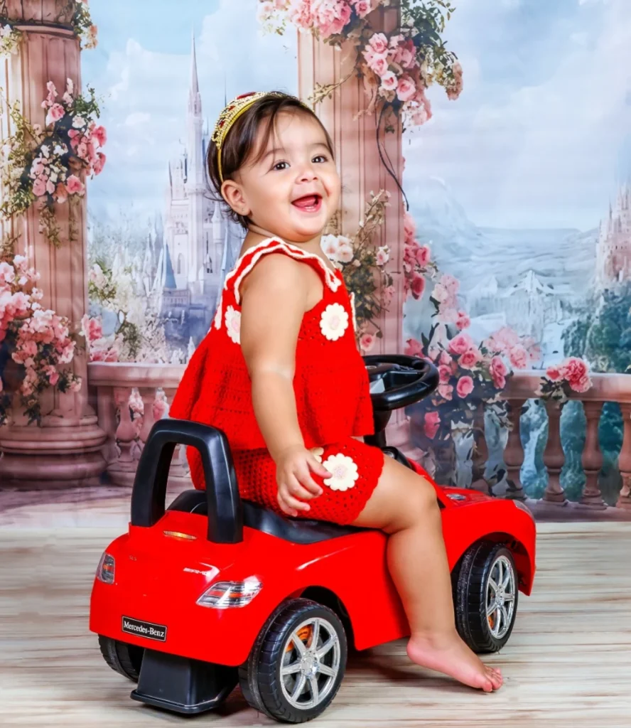 Niña con vestido rojo sobre un coche de juguete