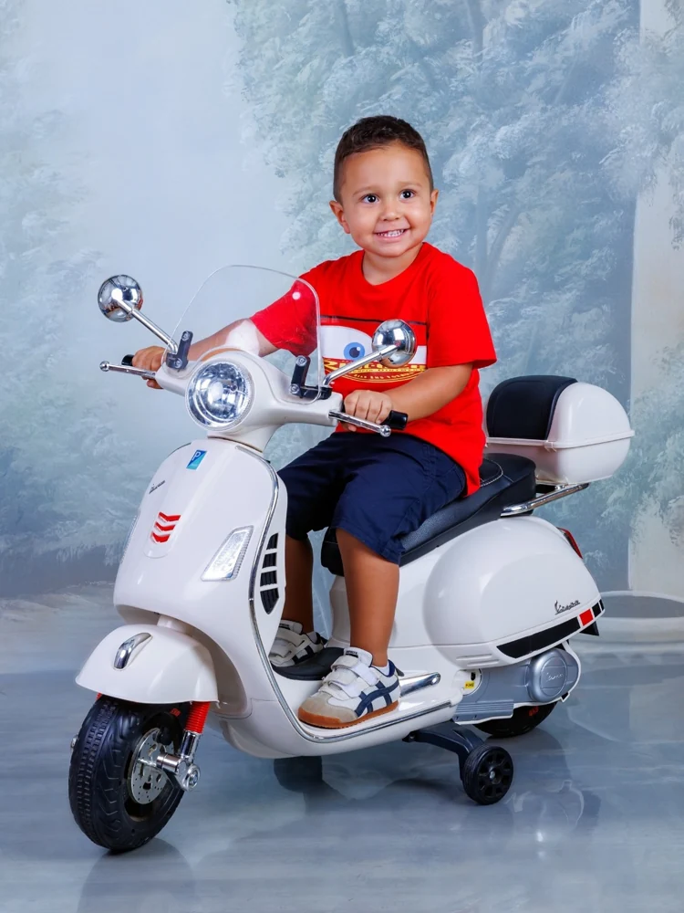 Niño con camiseta roja sobre una moto de juguete blanca en el estudio