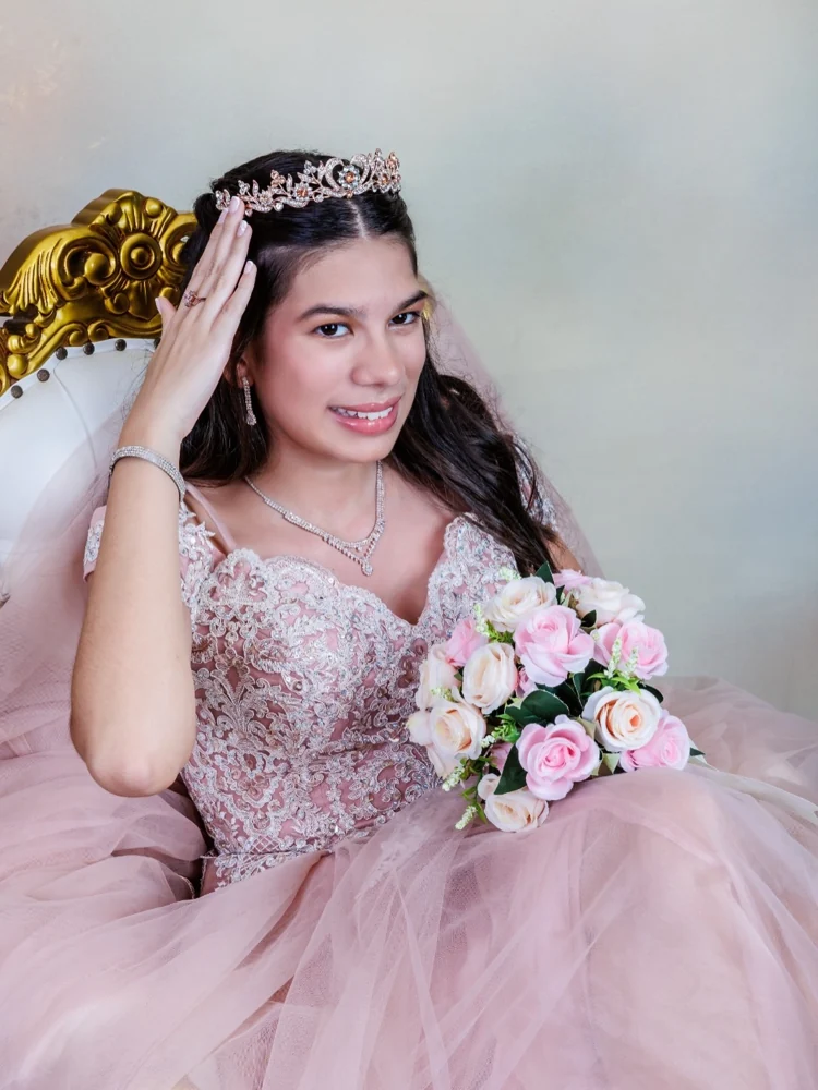 Quinceañera con vestido rosa, corona y ramo de flores en el estudio