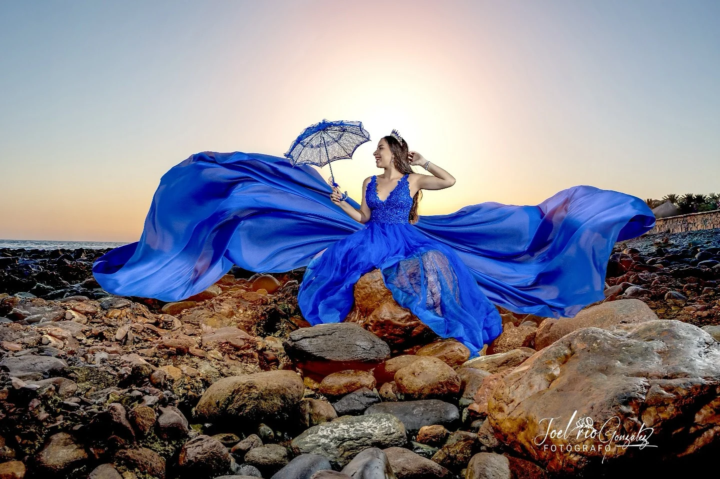 Quinceañera con vestido azul extendido sobre la costa rocosa de Gran Canaria