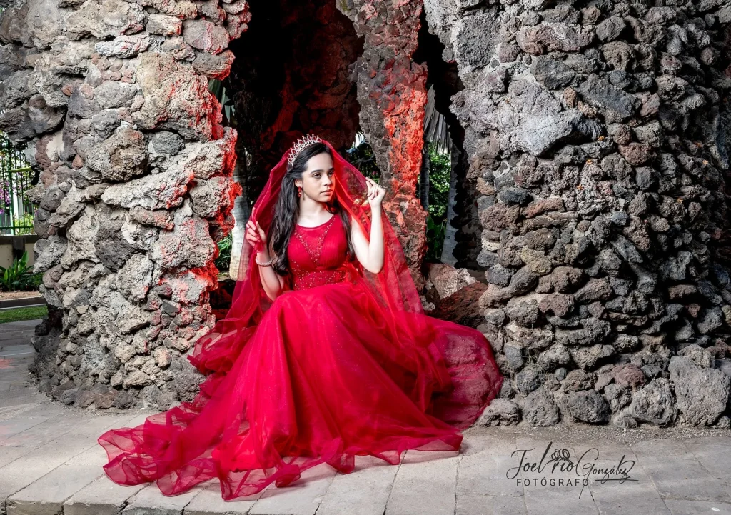 Quinceañera con vestido rojo junto a un muro de piedra