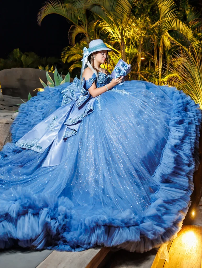 Quinceañera con vestido azul amplio entre palmeras iluminadas